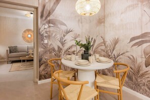 A dining area with a round table, four chairs, a vase with greenery, and a wall with a tropical leaf pattern. - Bali Blizz apartment 18 with sauna, whirlpool and terrace in Benz (Benz)