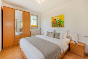 A bedroom with a bed, bedside tables, a wardrobe, a window, and a painting on the wall. - House Dünenwald 15 - Sunny Island: 57 m², terrace & 300 m to the sandy beach (Zinnowitz)