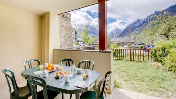 Tavolo apparecchiato per la colazione con vista sulle montagne, sedute all'aperto e un muro in pietra.