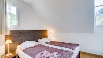 Un dormitorio con dos camas, cabecero de madera, mesita de noche con lámpara y ventana con vistas a las montañas.
