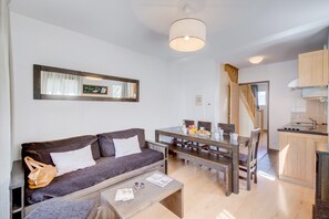 A modern living room with a sofa, coffee table, and dining table. There is a kitchen area with wooden cabinets and a staircase. - Loudenvielle Stay with Alpine Views (Loudenvielle)