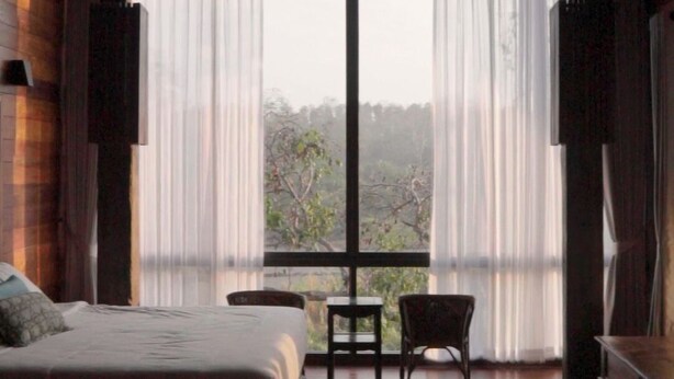 A bedroom with a large bed, a small table, a chair, and a view through large windows. - Baan Rim Doi Maerim (Mae Rim)