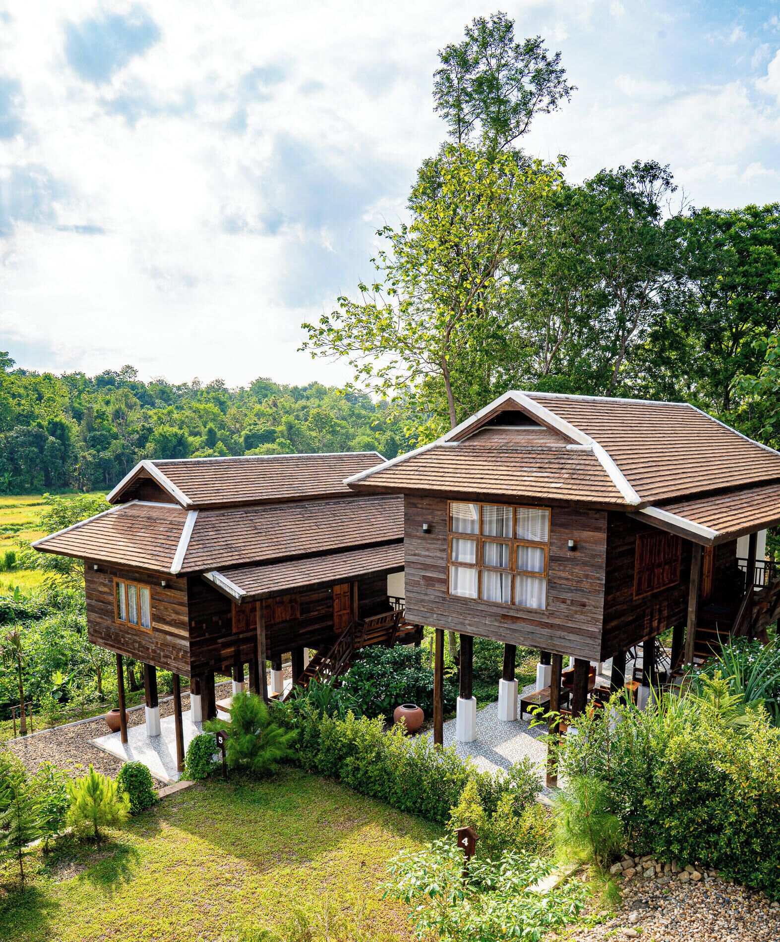 A wooden cabin with a sloped roof, elevated on stilts, surrounded by lush greenery and a clear sky.