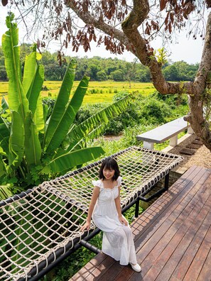 Una persona sentada en una hamaca sobre una cubierta de madera, con vistas a un paisaje verde.