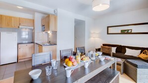 Una cocina moderna con armarios de madera, un área de comedor con mesa dispuesta para el desayuno, y un salón con sofá y cojines.