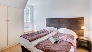 Un dormitorio con dos camas, cabecero de madera, armario y ventana que deja entrar luz natural.