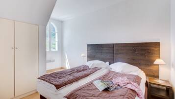 Une chambre avec deux lits, une tête de lit en bois, une armoire et une fenêtre qui laisse entrer la lumière naturelle.