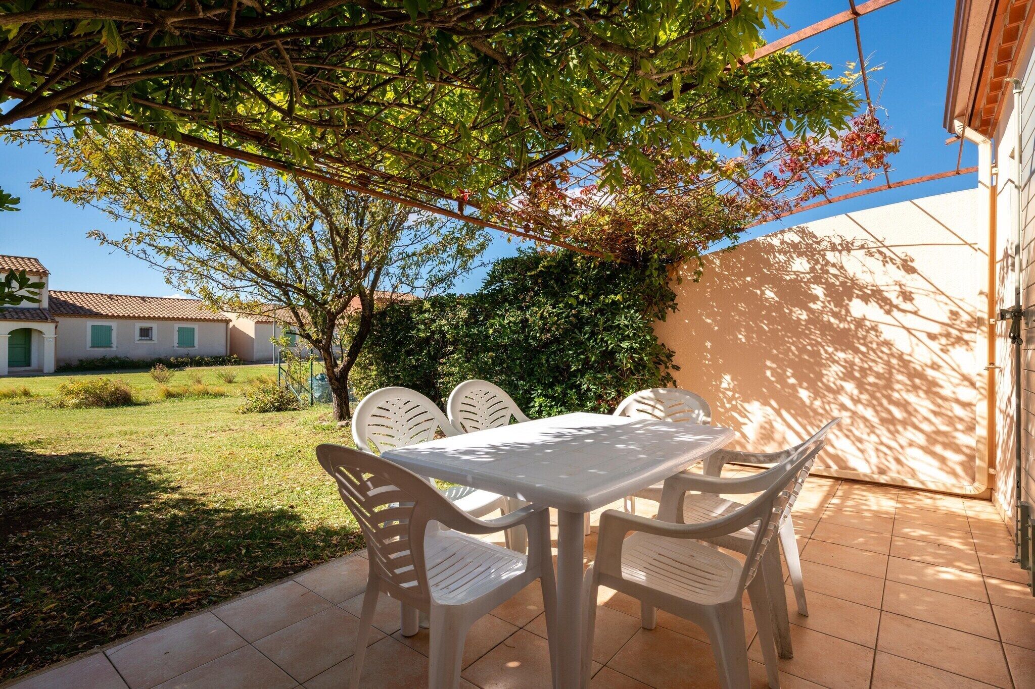 Une terrasse avec une table et des chaises, un arbre et un bâtiment en arrière-plan.