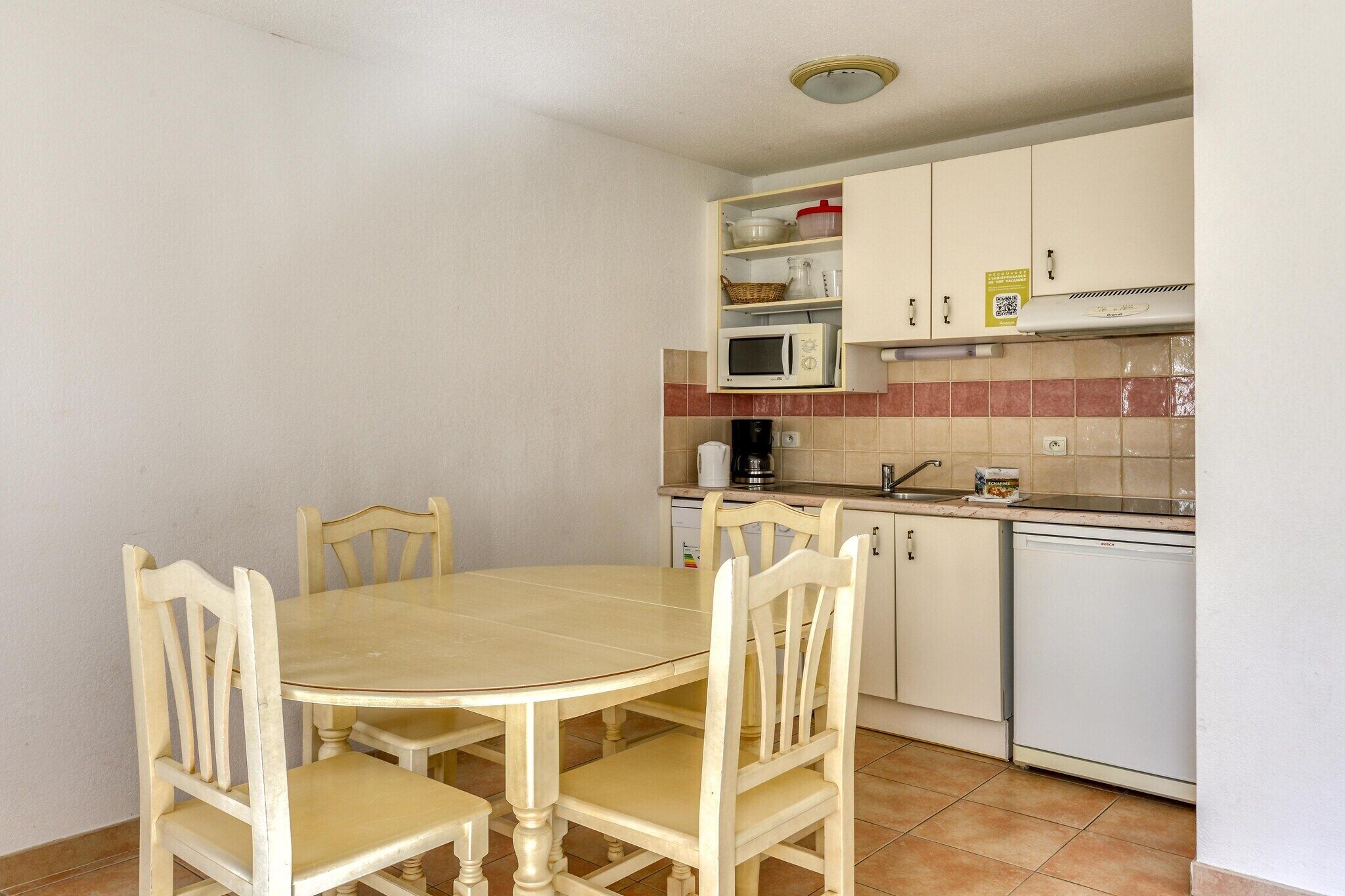 Uma cozinha compacta com uma mesa redonda e quatro cadeiras, micro-ondas, cafeteira e máquina de lavar louça.
