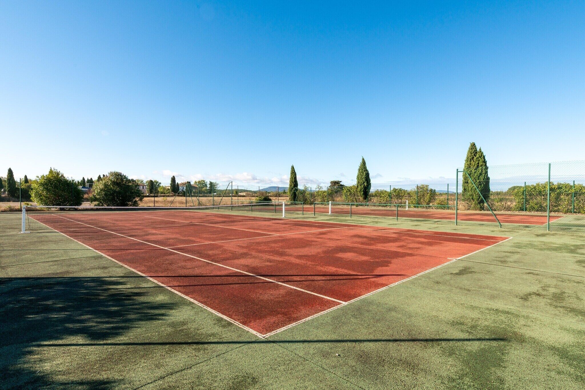Cancha de tenis con red, rodeada de árboles y un cielo despejado.