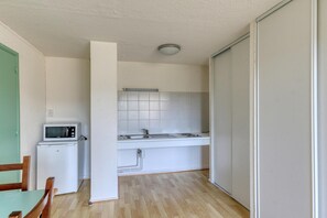 Une cuisine compacte équipée d’un four à micro-ondes, d’un évier et de placards, d’une table à manger avec des chaises, et d’une porte coulissante.