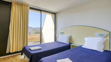 Habitación de hotel con dos camas, un ventanal grande y vistas al exterior.