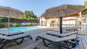 Ein Poolbereich mit Liegestühlen und Sonnenschirmen, eine Holzterrasse und ein Gebäude mit einer überdachten Terrasse.