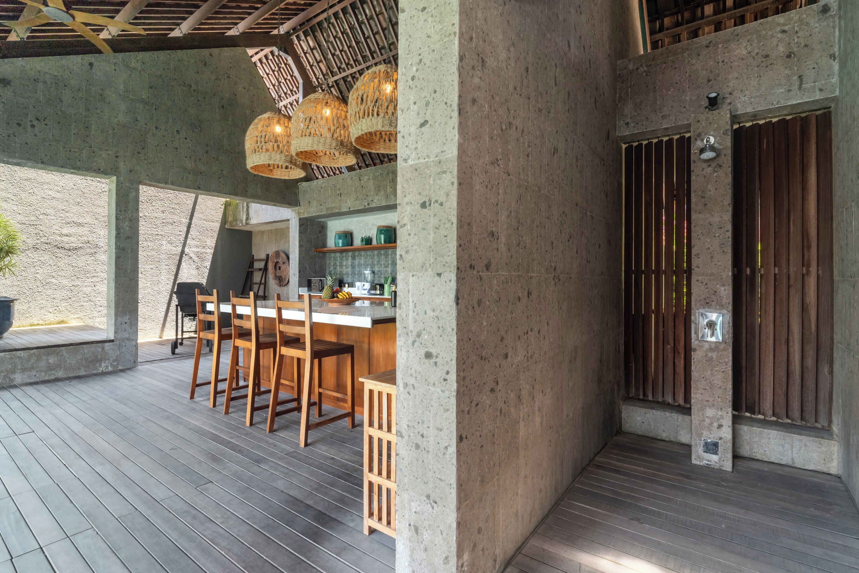 A modern kitchen with a bar area, wooden chairs, and a concrete wall.