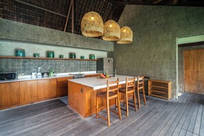 A kitchen with a large island, wooden chairs, a microwave, and a refrigerator. - Santos Cliff View  (Jimbaran)