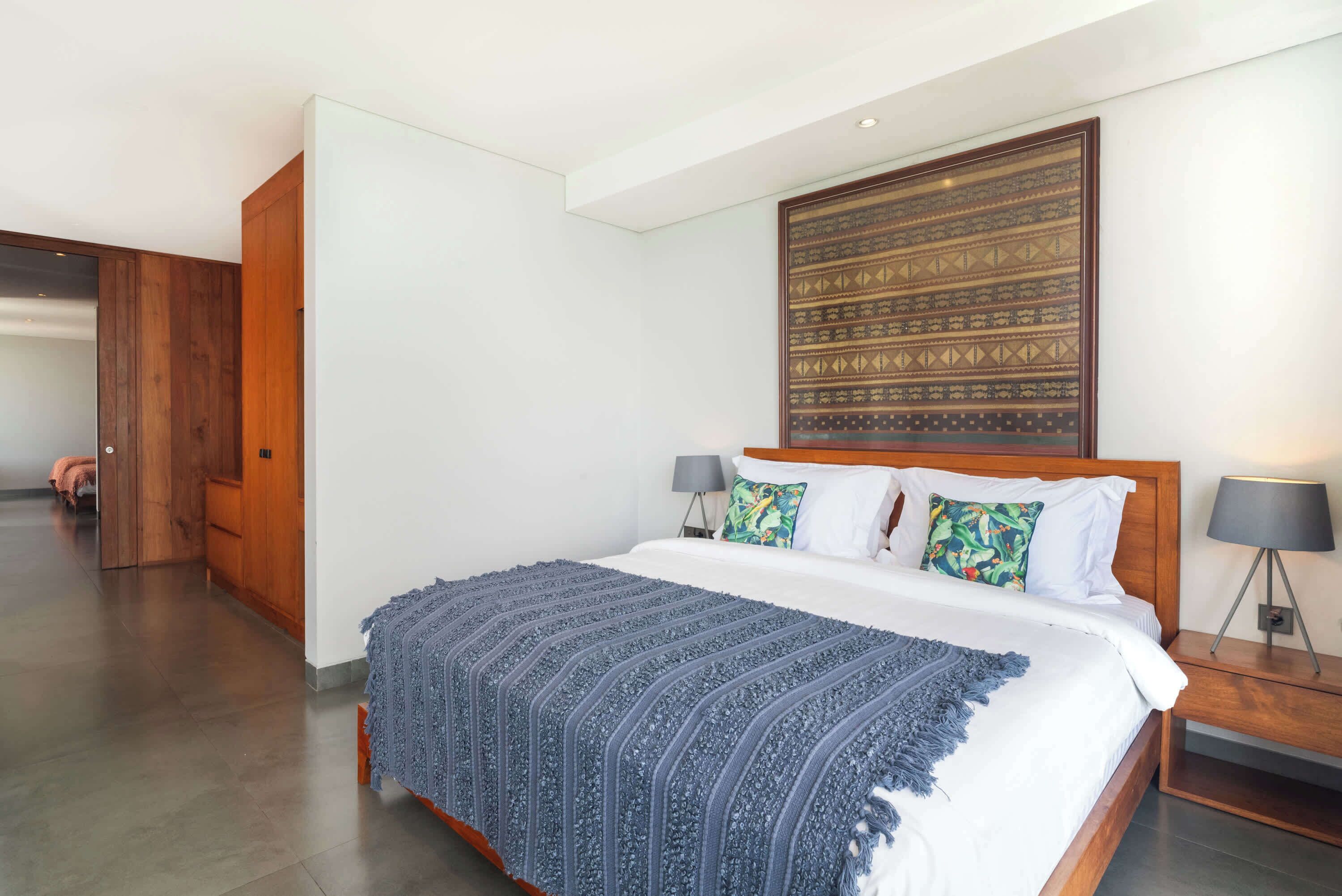 A modern bedroom with a large bed, wooden headboard, and a patterned wall hanging.
