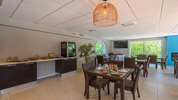 A modern kitchen with dark cabinetry, a dining area with wicker chairs, and a large window providing a view of greenery.