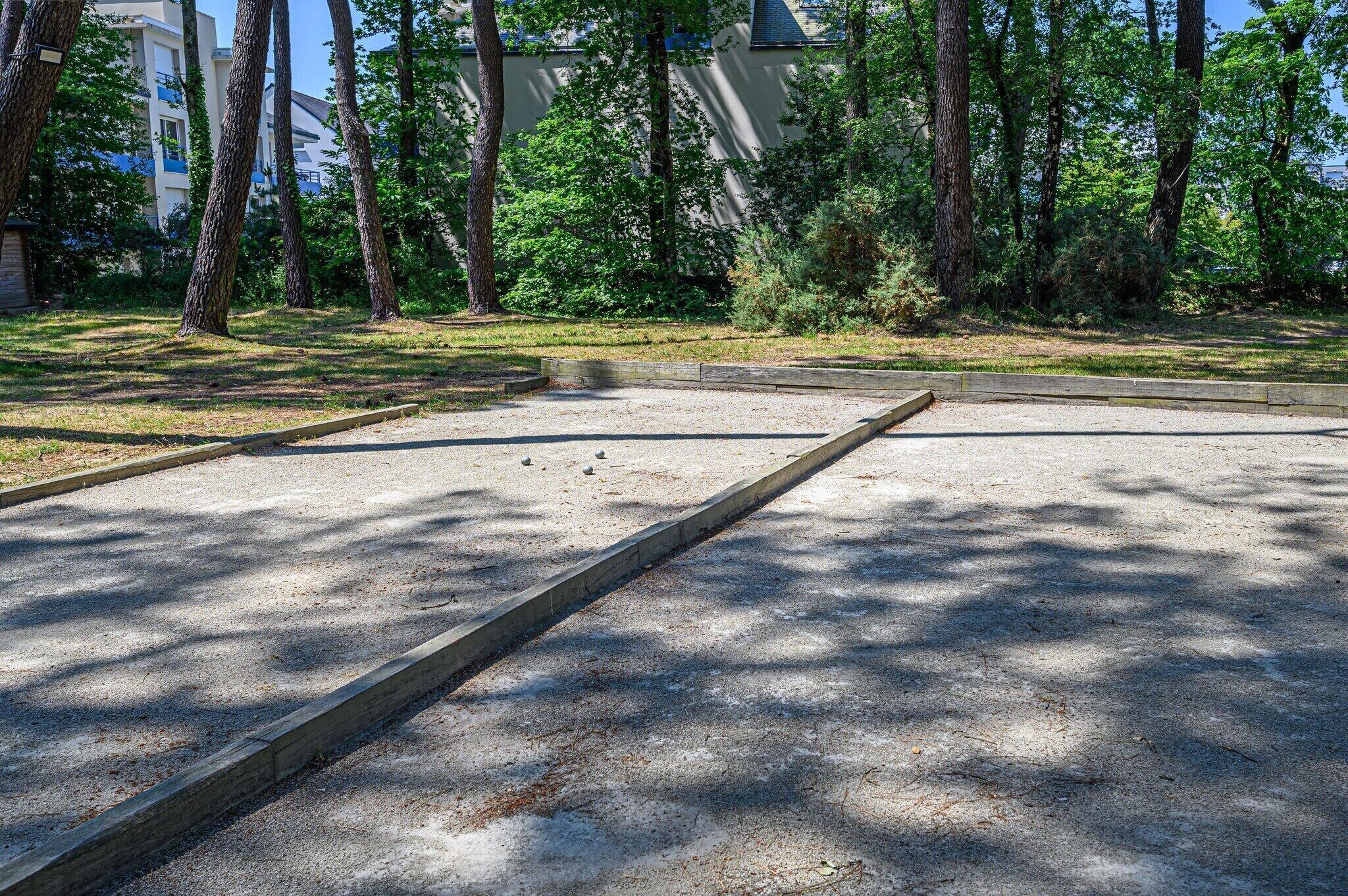 Un espace extérieur doté d’une surface en béton, entouré d’arbres et avec un bâtiment en arrière-plan.