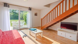 A living room with a sofa, a coffee table, a TV on a stand, a staircase, and a sliding glass door leading to an outdoor area. - Comfortable House Stay for 6 in Plescop (Plescop)