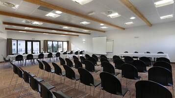 Une salle de conférence avec des rangées de chaises, un tableau blanc et un écran de projection.