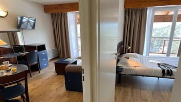 Un dormitorio con cama, escritorio y silla, televisor y ventana con cortinas.