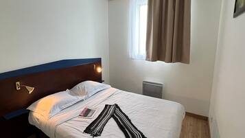 Une chambre d’hôtel avec un lit, une lampe de chevet, une fenêtre avec des rideaux et un radiateur.