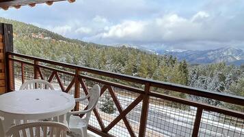 Un balcon avec une table et des chaises, donnant sur un paysage enneigé parsemé d’arbres et de montagnes.