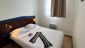 A hotel room with a bed, a bedside lamp, a window with curtains, and a radiator. - Modern apartment in Bolquère for family (BOLQUERE)