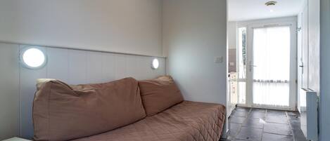Un dormitorio con cama, mesita de noche y puerta que da a un balcón.
