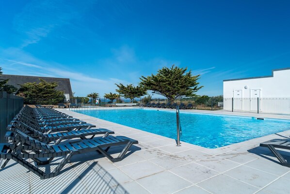 Une piscine avec des chaises longues, un ciel dégagé et un bâtiment blanc en arrière-plan.