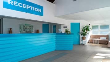 Una zona de recepción con un mostrador azul, un cartel que dice 'RECEPTION' y una planta.