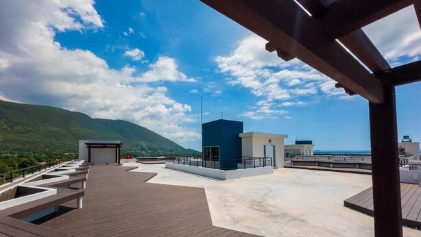 A wooden deck with benches, a small blue structure, and a view of the sea and mountains.
