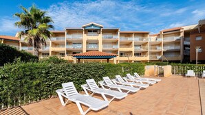 Un hotel con diversi balconi, una palma e lettini prendisole su un patio piastrellato.