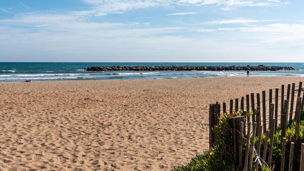 Una spiaggia sabbiosa con una recinzione in legno e un molo roccioso sullo sfondo.