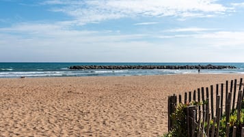 Ein Sandstrand mit einer Holzzaun und einem steinernen Wellenbrecher im Hintergrund.