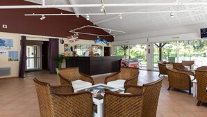 A hotel lobby with wicker furniture, a reception desk, and a large window offering a view of the outdoors. - Charming Apartment with Pool (SERIGNAN (HÉRAULT))