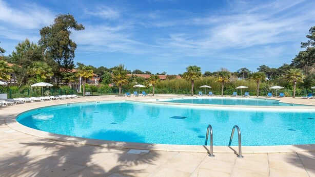 A large, clear swimming pool with lounge chairs and umbrellas, surrounded by palm trees and a clear sky. - Charming Apartment with Pool (SERIGNAN (HÉRAULT))
