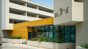 Een modern gebouw met een gele gevel en meerdere balkons, met een bord waarop 'DUUNE' staat.
