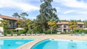A swimming pool with lounge chairs, palm trees, and a building with a tiled roof. - Coastal Retreat near Sandy Beach (SERIGNAN (HÉRAULT))
