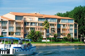 Un hôtel à plusieurs étages doté de balcons, avec un bateau amarré devant et des palmiers.