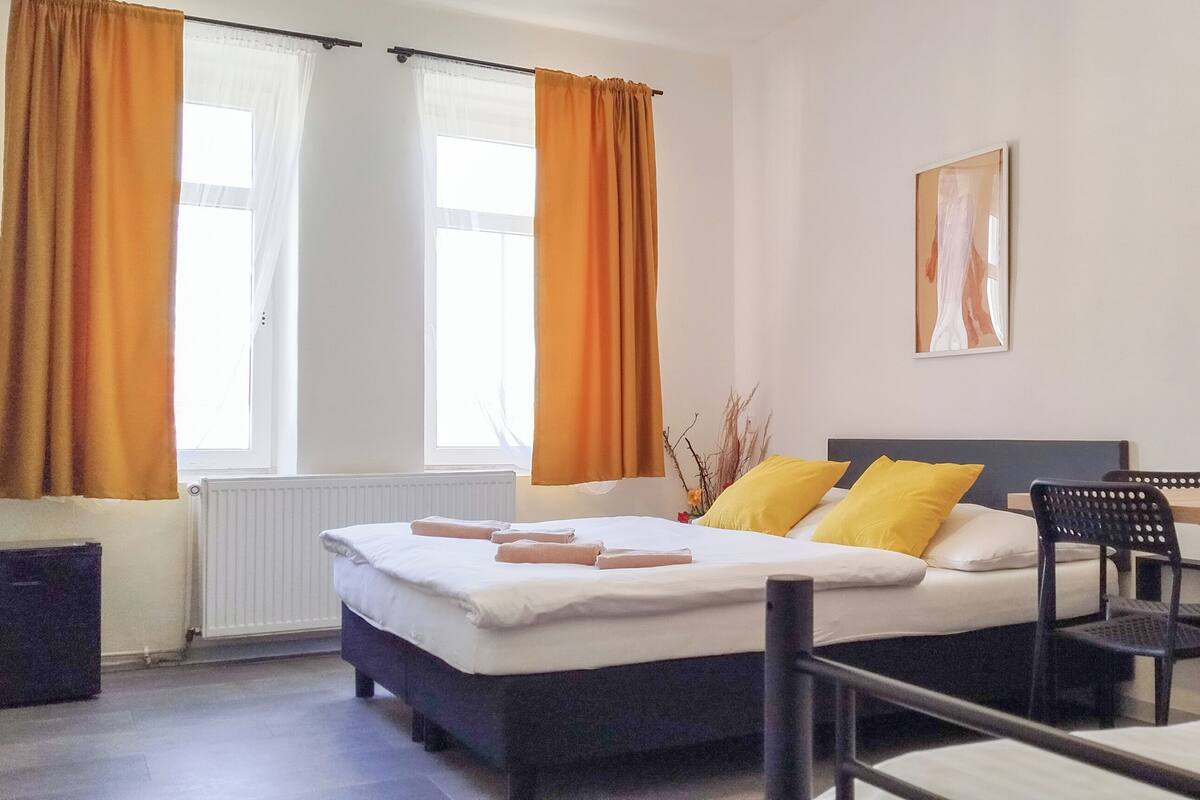 A hotel room with a bed, a desk, a chair, a mirror, and a window with curtains.