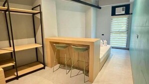 Una habitación pequeña con escritorio, dos sillas, estantería y ventana con persianas.