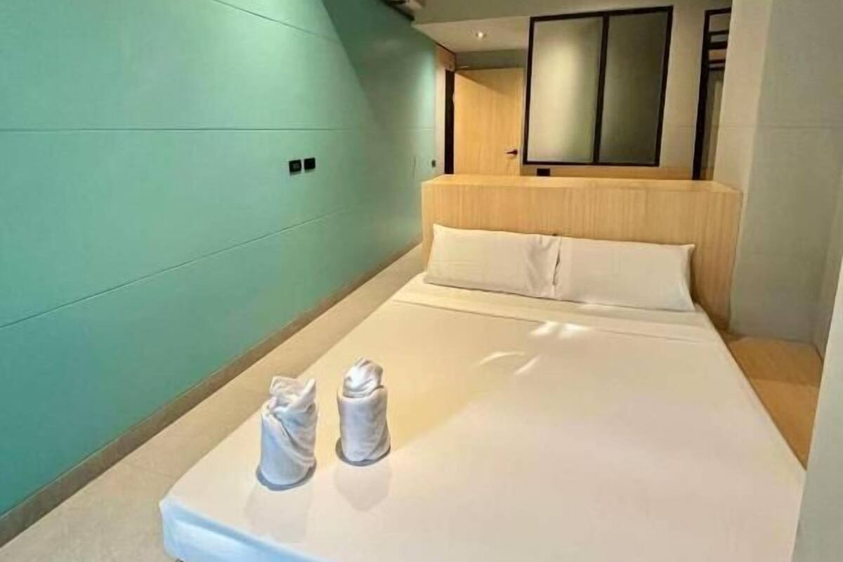 Una habitación de hotel moderna con una cama, un cabecero de madera, un espejo grande y una pared de acento color aguamarina.
