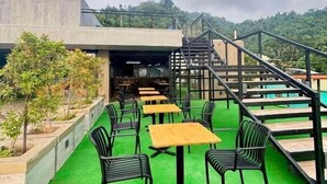 Un espacio al aire libre con mesas y sillas, una escalera y vista a un edificio en el fondo.