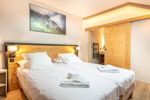 Ein Doppelbett mit weißen Leinen, ein Holz-Kopfteil, Nachttischlampen, ein Gemälde an der Wand und ein Holzschrank.