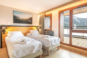 A bedroom with two beds, a wooden headboard, a large window with a mountain view, and a painting on the wall. - Alpine Home with Wellness Access (VAUJANY (ISERE))
