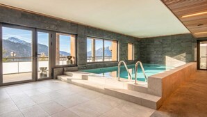 En moderne indendørs swimmingpool med store vinduer, udsigt til bjerge og flisegulv.