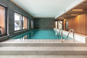 Ein Hallenbad mit freiem Blick auf das Wasser, Stufen zum hineingehen und einer Holzverkleidung an einer Seite.