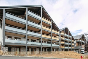 Een meerlaags gebouw met balkons, een gevel van natuursteen en een bergachtige achtergrond.