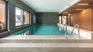 Piscina interna con vista chiara sull'acqua, scalini d'accesso e una parete in legno su un lato.